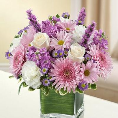 This bouquet features a lavender and white arrangement of roses, stock, liatris, cremones, carnations, daisy poms and monte casino, accented with variegated pittosporum
artistically designed by our florists in a classic clear glass cube vase lined with a Ti leaf ribbon.