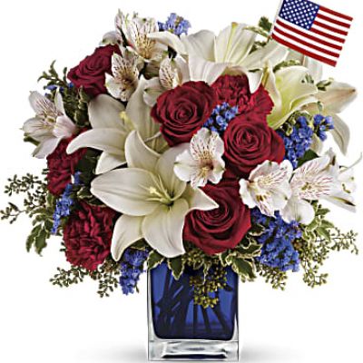 A patriotic pick to send a brave veteran, decorate your Fourth of July picnic, or celebrate Memorial Day. Lush red, white and blue flowers are presented in a deep blue glass cube vase along with an American flag.
Red roses, white asiatic lilies, white alstroemeria, blue statice and red carnations are gathered with green pitta negra, seeded eucalyptus and a small American flag in a cobalt blue glass cube.